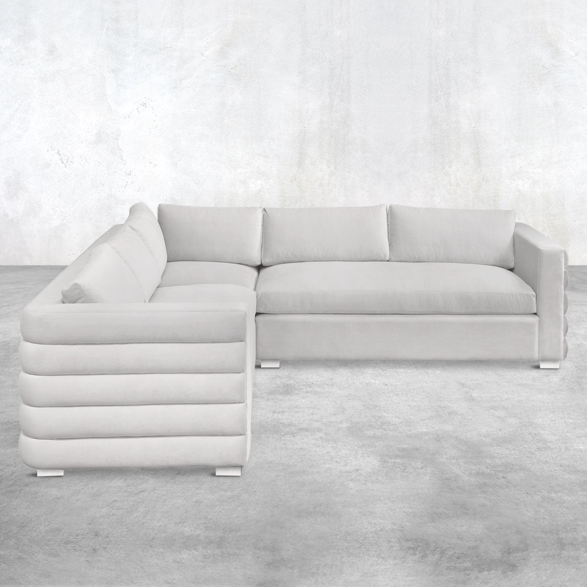 Light gray L-shaped three-piece sectional with pin feet, a pillow back, straight arms and horizontal channel-tufted upholstery on the outside.