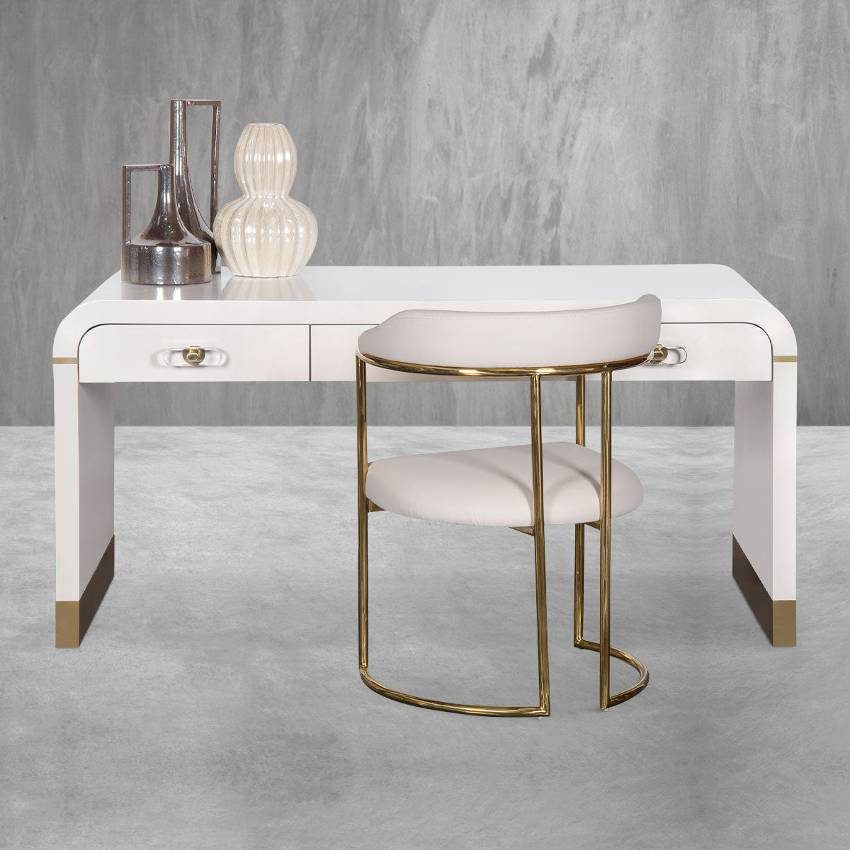Modern white desk with three drawers, curved edges, solid sides and polished brass accents along with a matching white and brass chair and desk decor.
